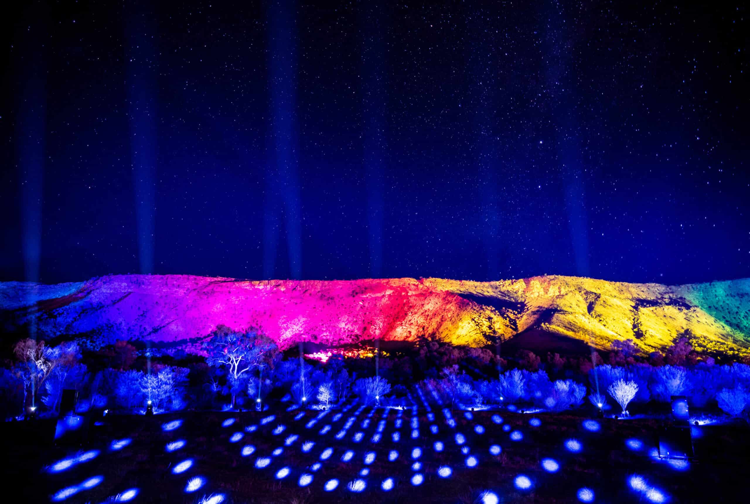 A photo of a hill, lit up with various bright colours, at night time.